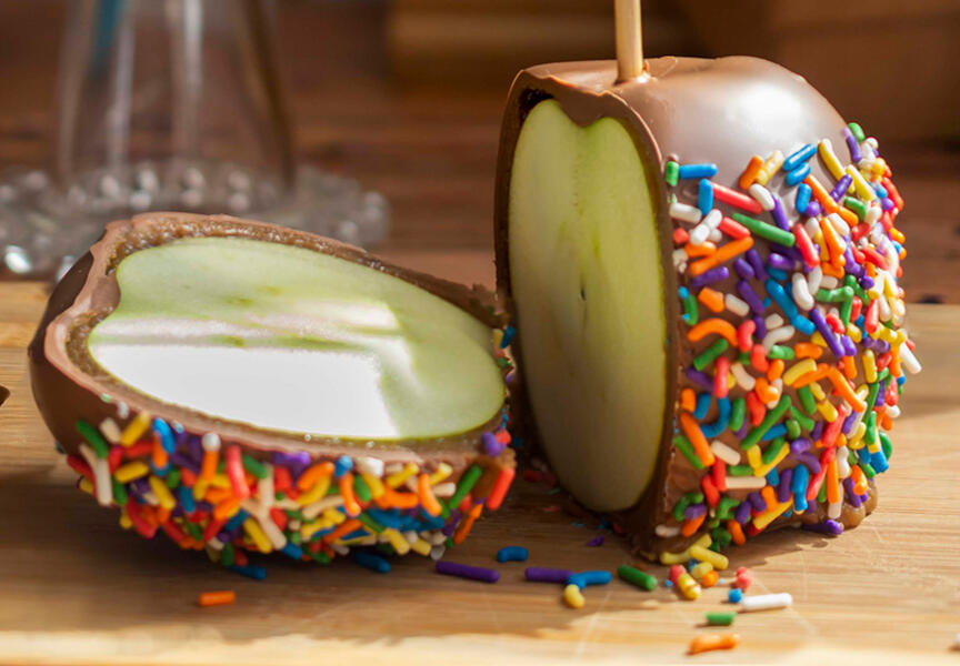 An apple coated in chocolate with rainbow sprinkles.